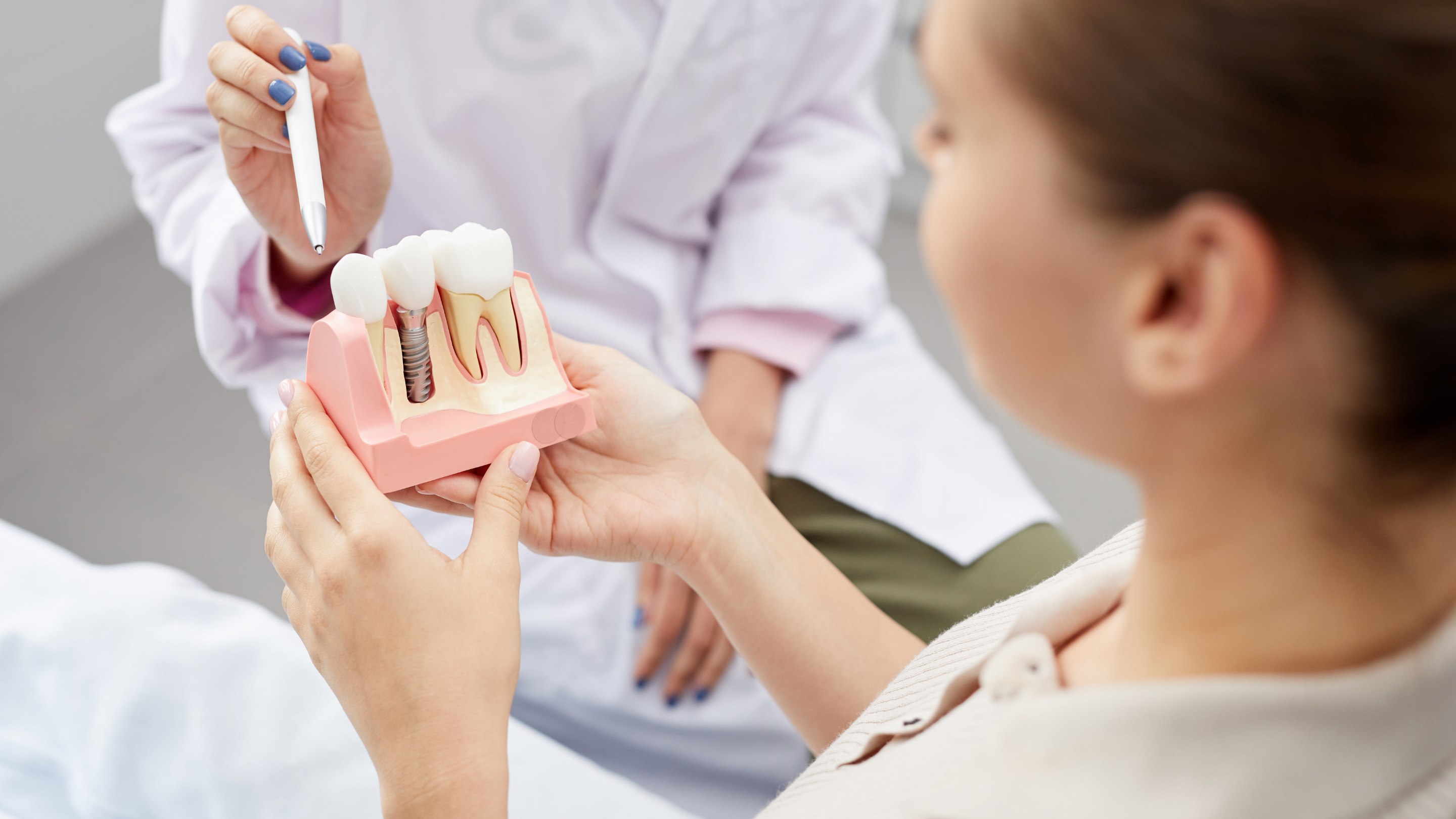 A dentist explaining a dental implant using a jaw model