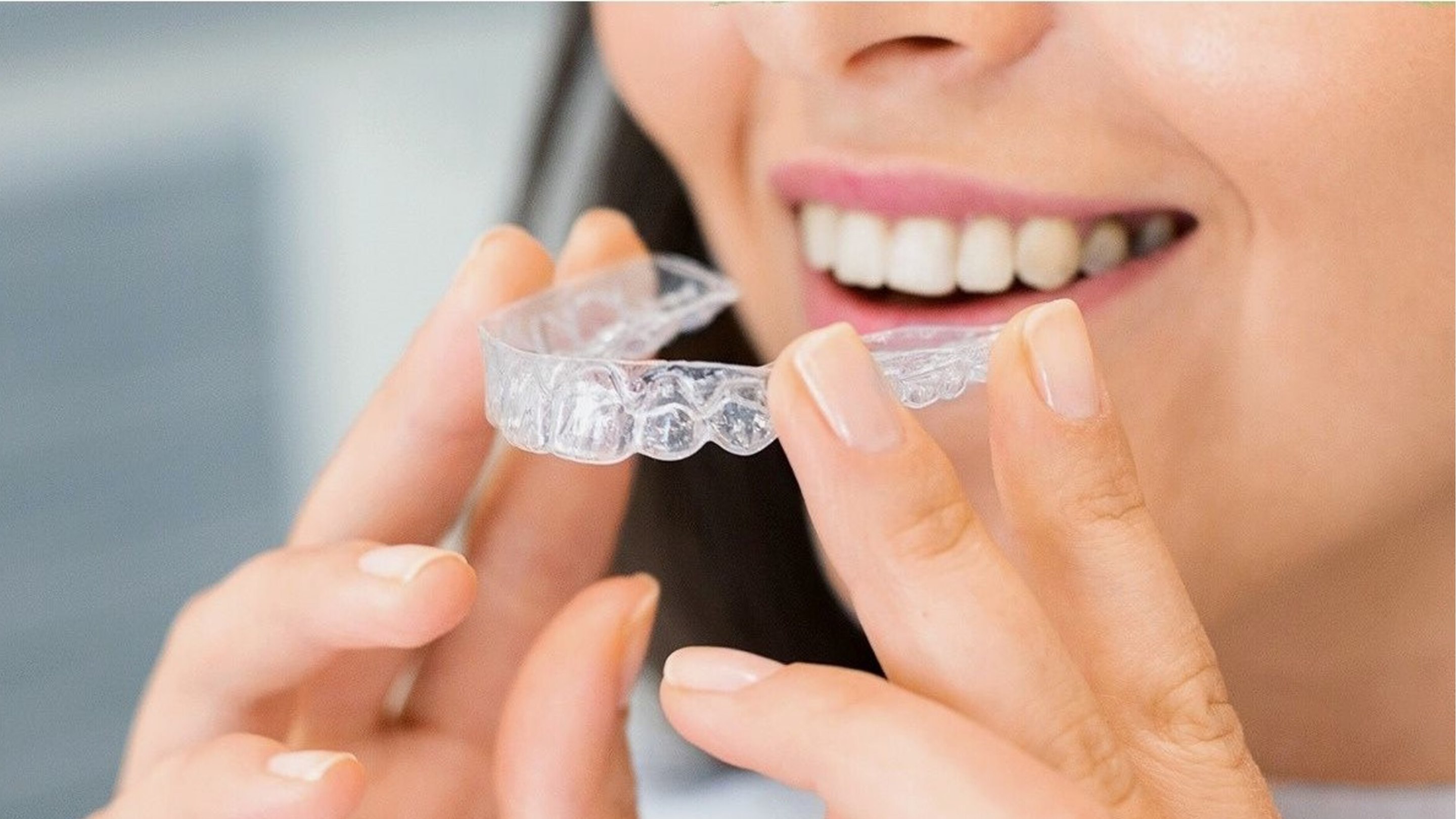 A clear removable dental aligner held in front of a smile